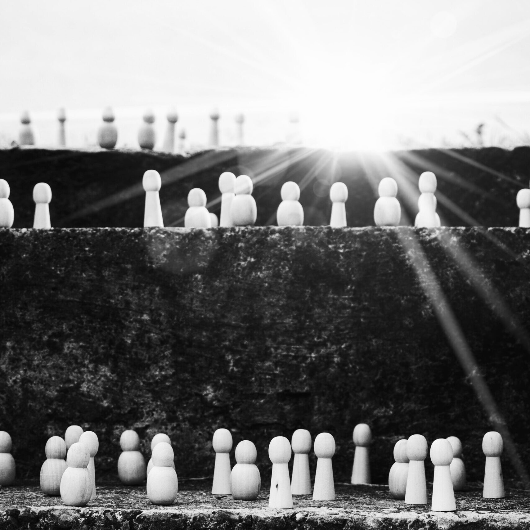 Black and white image of pions in different shapes and sizes standing on three different levels, with a bright sun in the background