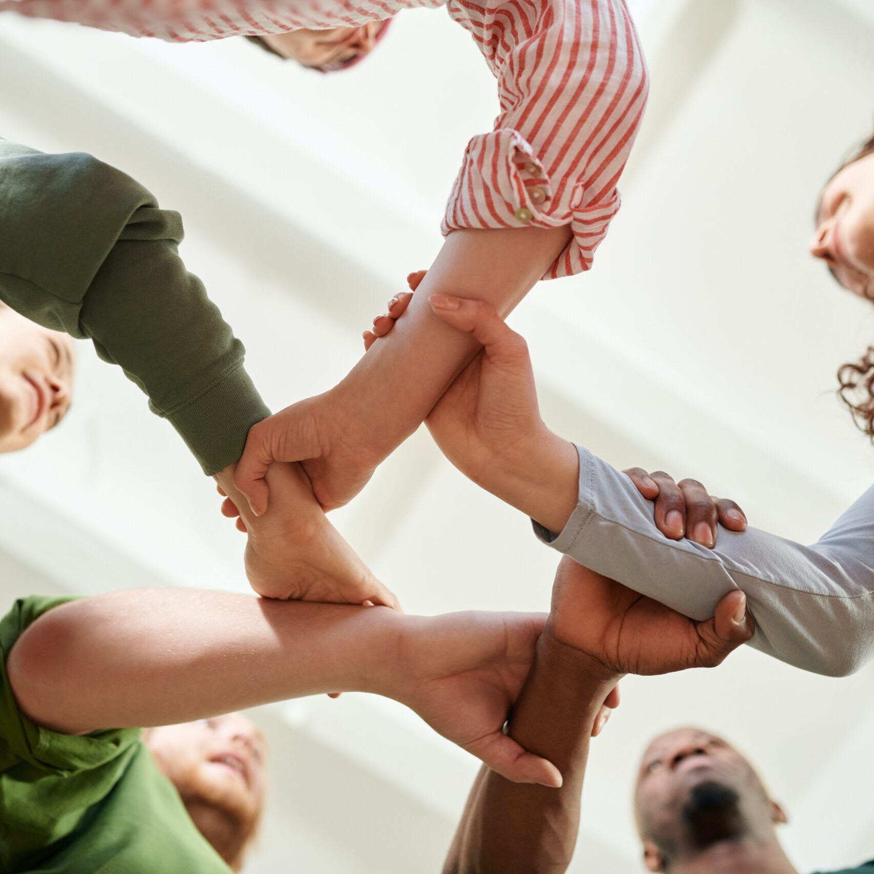 Five people of different genders and skin colors holding wrists to form a dynamic circle, shot from beneath