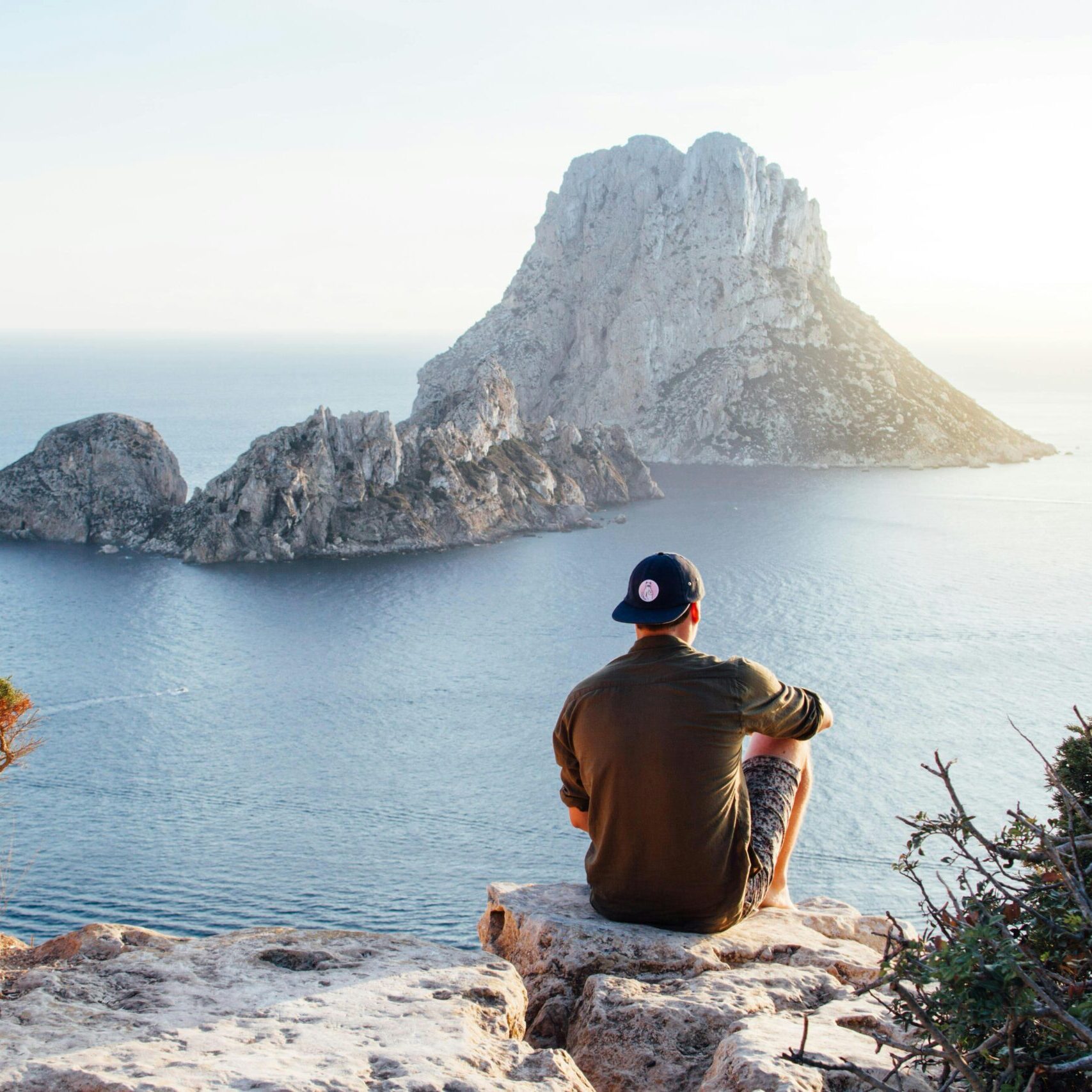 Man sitting with his back to the camera, overlooking a beautiful rocky bay on the ocean side