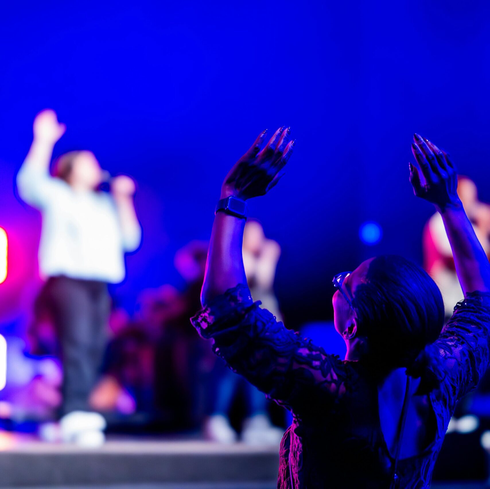Woman in the audience raising both her hands in reaction to speaker on stage