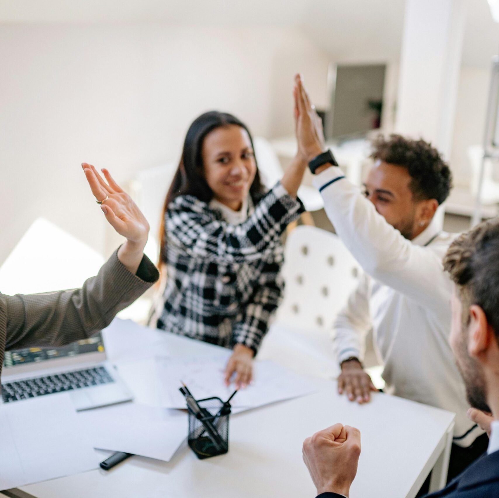 A group of four diverse young people in an office setting giving each other high fives