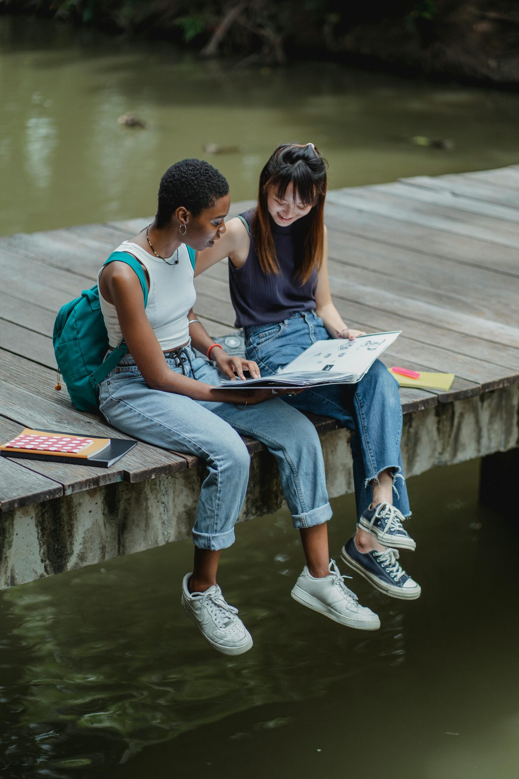 Two women of color sitting on a deck over a river, studying together