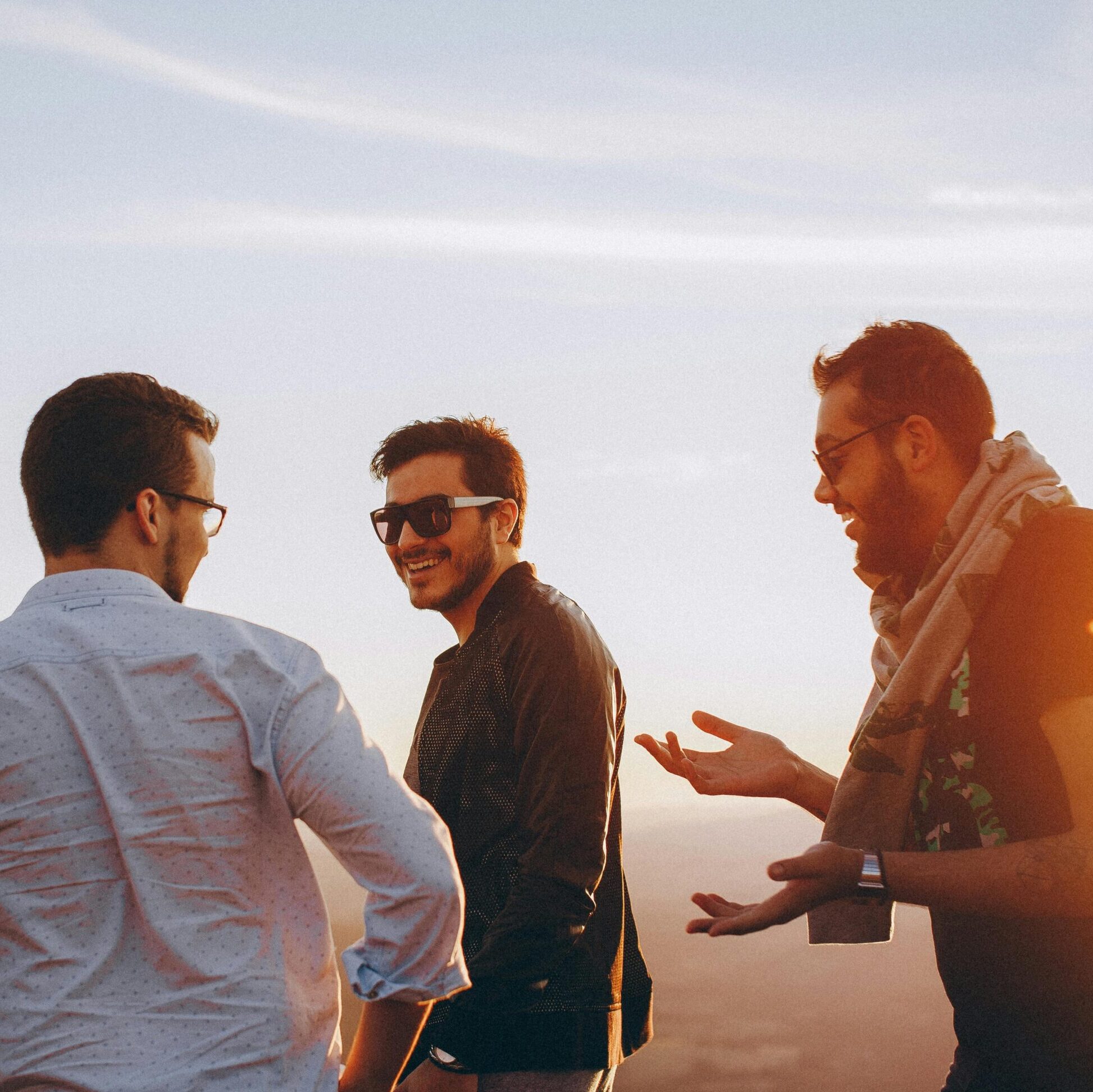 Three men talking out in the sun against the backdrop of a clearblue sky