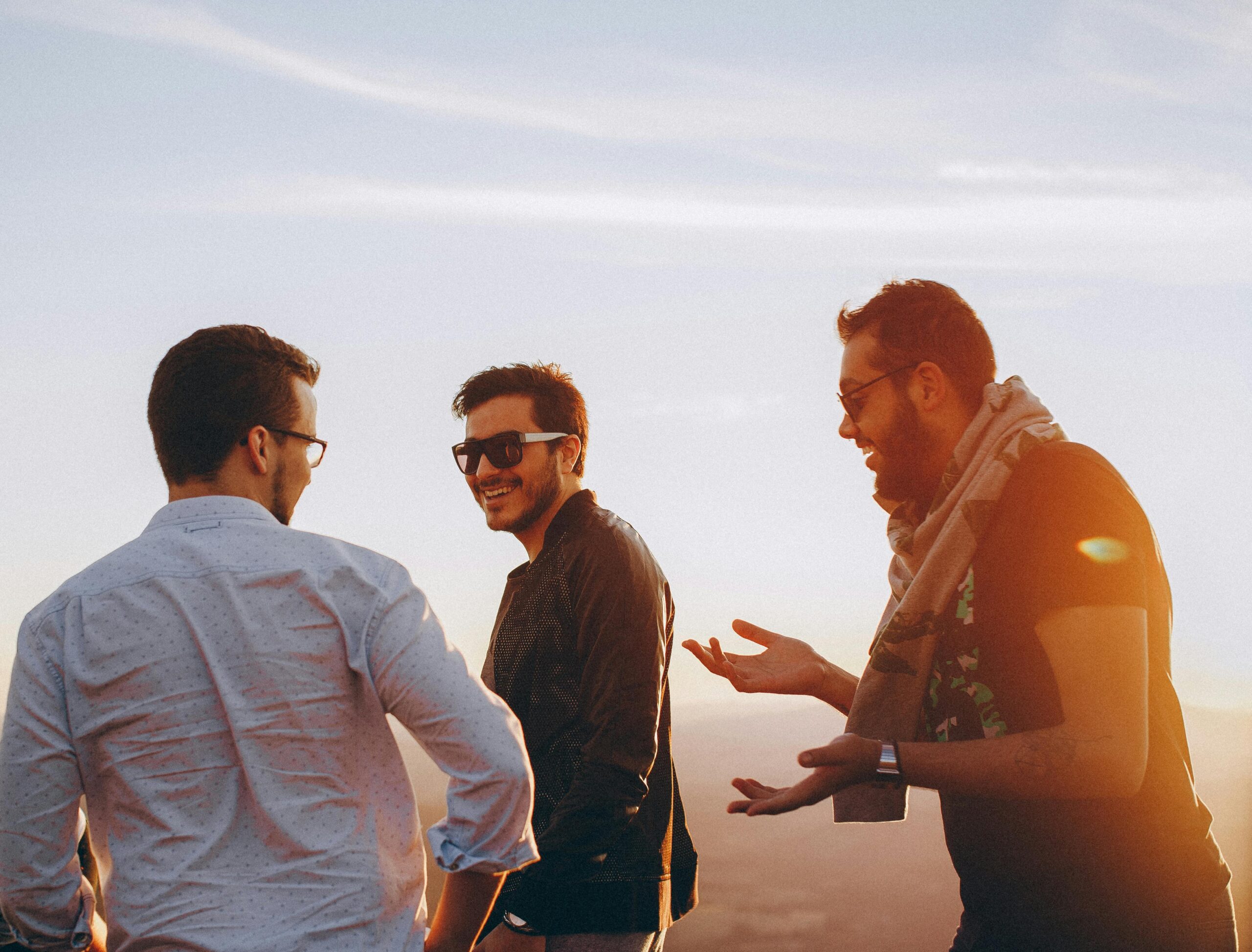 Three men talking out in the sun against the backdrop of a clearblue sky
